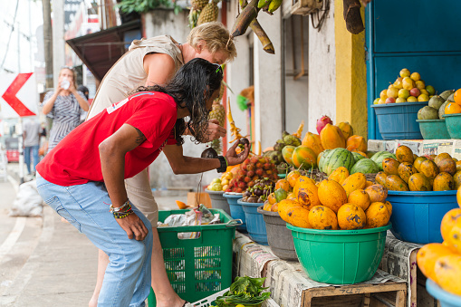 A local man is helping a European woman, a tourist, to pick fresh fruits on a street market in Bentota, Sri Lanka