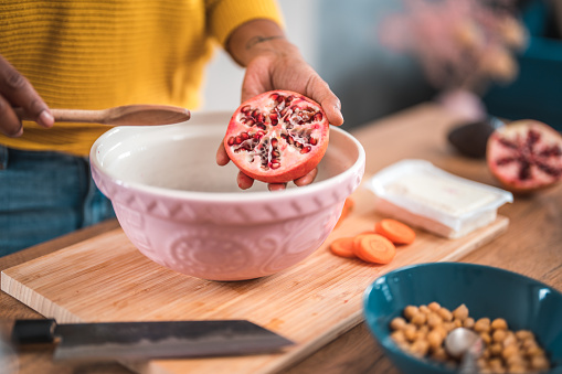 Close-up photo of a woman expertly extracting pomegranate seeds into a ceramic bowl using a wooden spoon.
