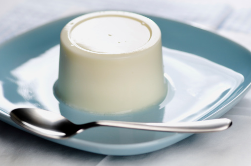 Plain panna cotta on a blue plate with spoon