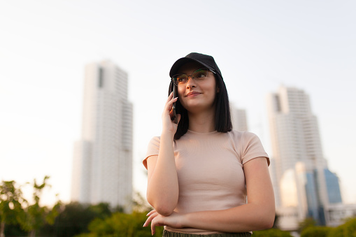 Beautiful girl with dark hair wearing cap and talking on a phone. Three skyscrapers in the background.