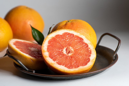 Grapefruit in a metal plate. Slices and whole fruits of juicy fresh grapefruit on a light background