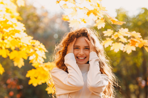 Smiling young woman enjoy the autumn weather in the parkland with the yellow leaves at branches