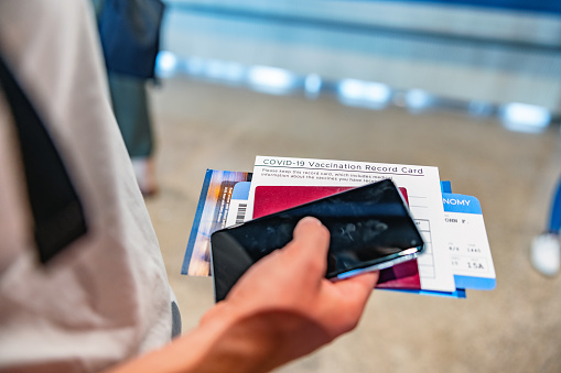 A man's hands holding tightly onto his travel plans - passport, plane ticket, and phone - as he waits for his departure at the airport terminal.