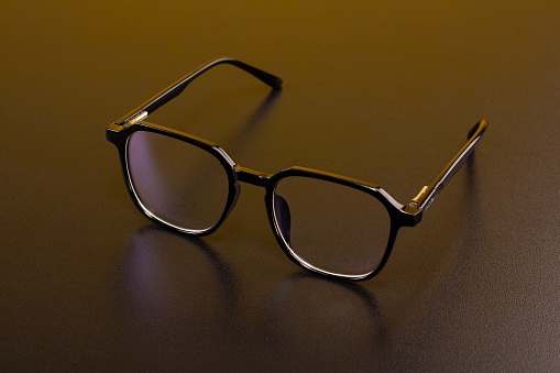 Glasses with modern and elegant frames on a dark background, with a reflection in the base in a studio photo