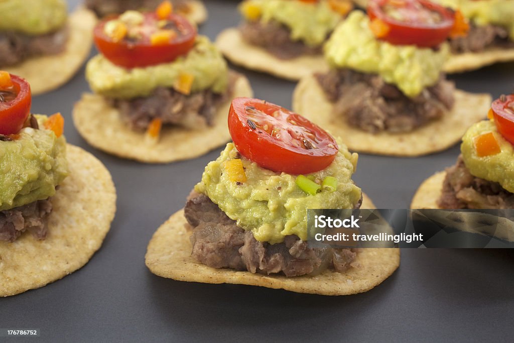 Mexican Bites Nachos Appetiser Finger Food "Spicy Mexican party food, corn chips topped with refried beans, avocado and tomato salsa." Avocado Stock Photo