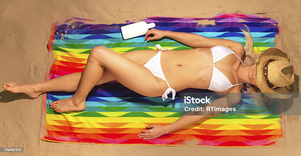 Woman sunbathing in bikini with straw hat "A slim blond woman lying on her back sunbathing on a beach wearing a white bikini with straw hat over her face, shot from above." Beach Stock Photo