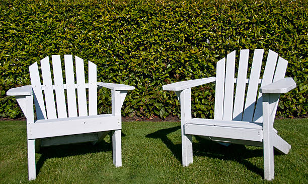 Close up of two white adrinodack chair on a lawn.