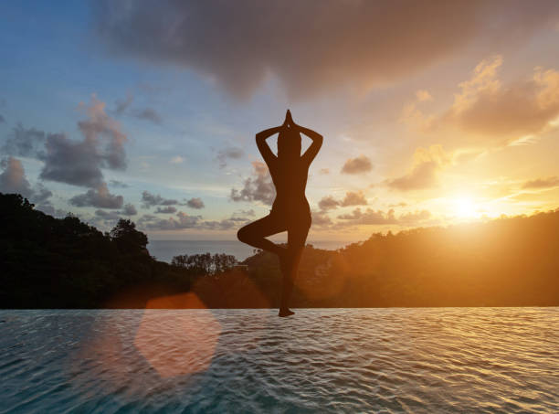 une femme faisant une pose d’arbre au bord de l’étang. concept, silhouette, romantique, bonheur, repos, vacances, soins de santé - waters edge lake beach tree photos et images de collection