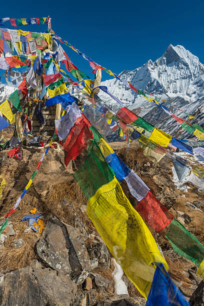 Colourful Buddhist prayer flags flying below Annapurna peak Himalayas Nepal Colourful Buddhist prayer flags fluttering in the breeze from a shrine at Annapurna Base Camp in front of the snow capped summit pyramid of Machapuchare (6993m), the iconic unclimbed peak and sacred mountain deep in the Annapurna Conservation Area of the Nepal Himalaya. ProPhoto RGB profile for maximum color fidelity and gamut. annapurna circuit photos stock pictures, royalty-free photos & images