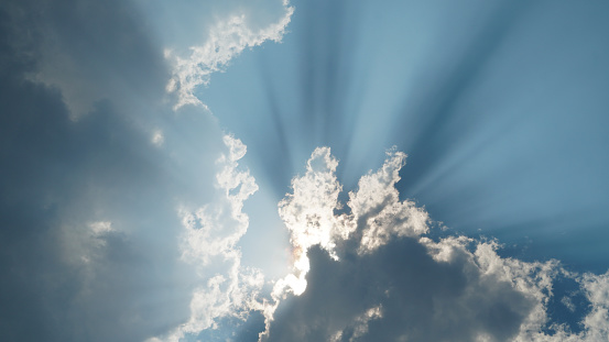 Sun rays shines through thick clouds on several sides, revealing a straight line between dark and light on the surface of the blue sky.