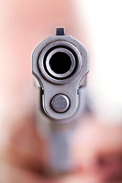 Barrel of a Gun Extreme close up macro shot of the dangerous front edge of a 9mm handgun. Even though the depth of field is extremely shallow, an obscured shape of a head and hands holding the gun can be seen in the background, defocused. gun barrel stock pictures, royalty-free photos & images