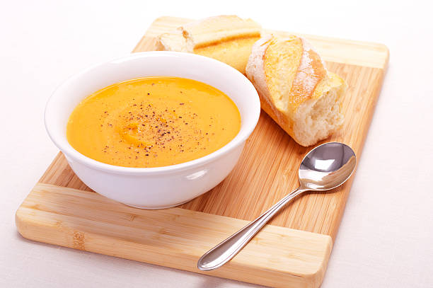 Orange soup served on a wooden board with fresh bread stock photo