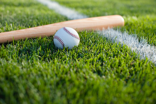 Baseball and bat on grass field with white stripe. Low angle view with defocused foreground and background.Some others you may also like: