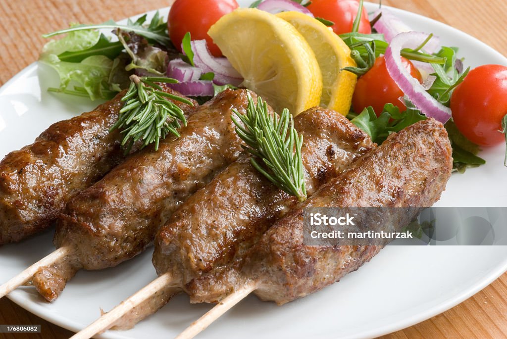 Four lamb kebabs served with a side salad and lemon wedges Lamb kebab with vegetable salad on a plate Arugula Stock Photo