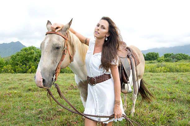 beautiful young woman holding a horse by the rains in a Kauai ranch