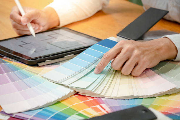 istock Designer hand choosing and pointing at color swatch or rainbow colour palette guide while working on digital tablet. Selection coloring for architecture and interior design work. 1768084059
