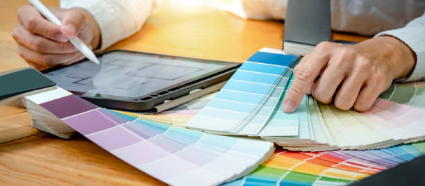 istock Designer hand choosing and pointing at color swatch or rainbow colour palette guide while working on digital tablet. Selection coloring for architecture and interior design work. 1768088848