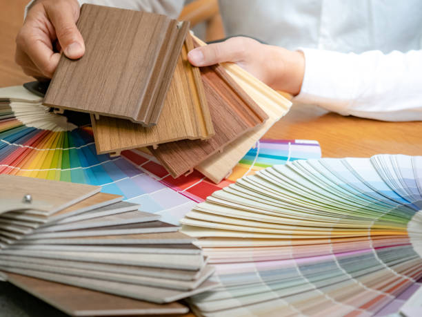 istock Designer hand choosing wood laminate material samples with color swatch and wooden tile texture collection nearby. Catalog guide for interior architecture and furniture design work 1768091894