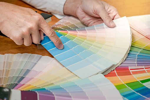 Designer hand choosing and pointing at color swatch samples catalog or rainbow colour palette guide for selection coloring on architecture and interior design work.