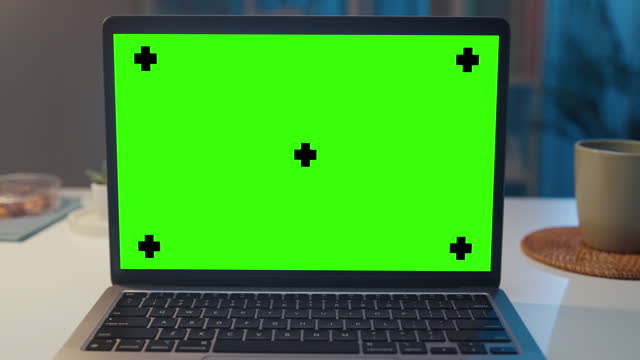 Closeup of laptop with mock-up green screen in living room at home night. Chroma key technology, Marketing design.