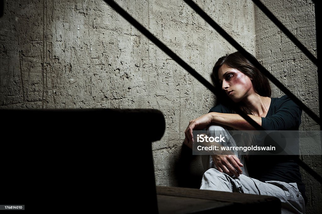 Used and abused; domestic violence concept Abused woman in the corner of a stairway comforting herself Domestic Violence Stock Photo