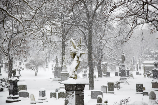 Sculpture of a snow covered angel at the cemetery on a winter day
