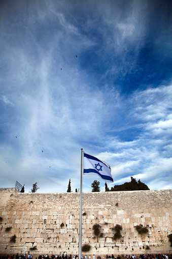 Israel flag fluttering in the wind in front of the holy Wailing Wall, one of the most sacred places to the Jewish people.