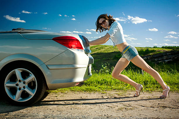 Beautiful young woman trying to repair her car in rural scenery.