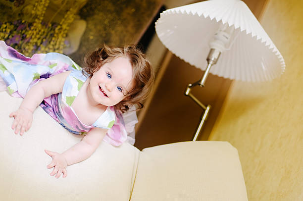 cute baby girl well-dressed lies on sofa near lampshade and smile