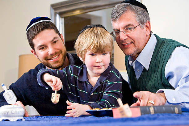 A father and grandfather teaching a boy to spin a dreidel Boy with father and grandfather spinning dreidel, celebrating Hanukkah yarmulke photos stock pictures, royalty-free photos & images