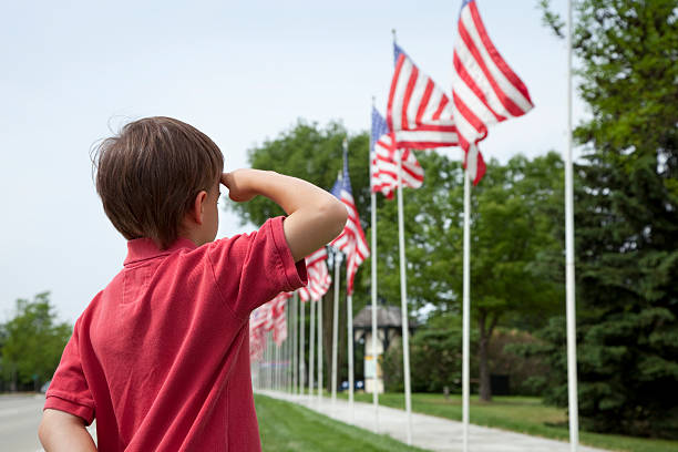 młody chłopiec salutes flagi na memorial day wyświetlania - child patriotism saluting flag zdjęcia i obrazy z banku zdjęć