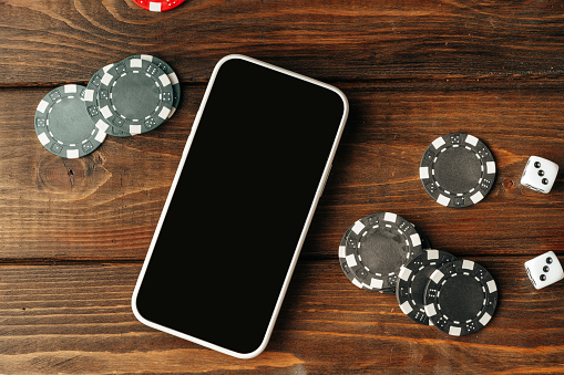 Poker chips and smartphone on wooden table close up