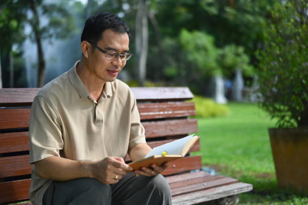 istock Pleased middle age man reading favorite novel while sitting on bench at public park 1768222850