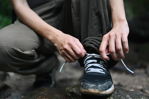 Female hiker tying shoelaces, getting ready walking in forest. Active life, adventure and healthy lifestyle.