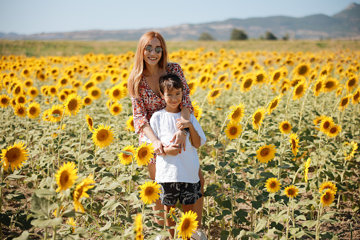 Happy mother with the son in the field with sunflowers. Mom and baby boy having fun outdoors. family concept.