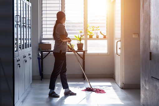 Janitor woman mopping floor in hallway office building or walkway after school or classroom with blank copy space. Housekeeper working job with sun light background.