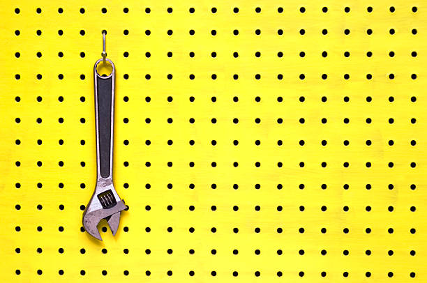 una chiave regolabile è appeso a un gancio in giallo pannello traforato - pegboard foto e immagini stock