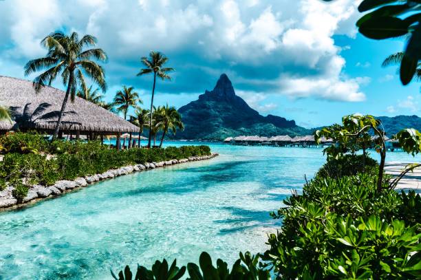 the beautiful water view of a lagoon and mountains at moored houses in bora An idyllic view of a lagoon surrounded by mountains and colorful traditional houses moored along the shoreline bora bora mountain stock pictures, royalty-free photos & images