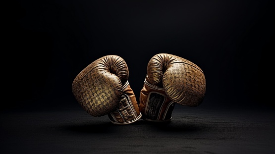 Two black boxing gloves on a black wall, hanging in close proximity to each other