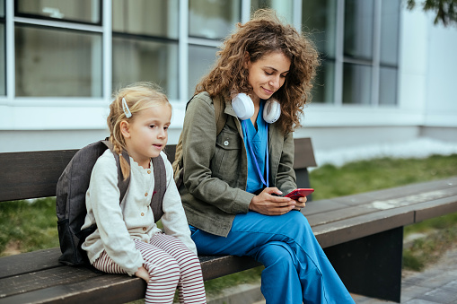 Mother and daughter are sitting on a bench, mother is using a mobile phone