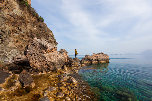 A woman is standing on the rocky shore, watching the sea view.