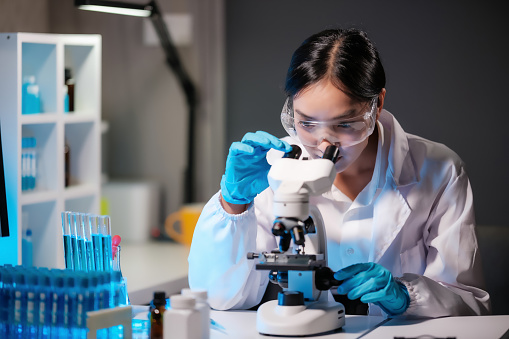 Asian female scientist looking under microscope, analyzes petri dish sample. specialists working on medicine, biotechnology research in advanced pharmacy lab, Medical development laboratory.