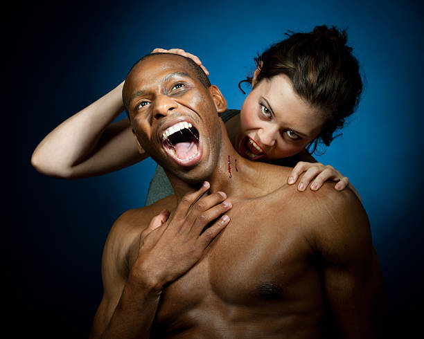 Vampire Woman Enjoys the Blood Brunette vampire makes challenging eye contact with the viewer as she pulls away from a bite she has just put on her unwilling victim. Black man screams in terror and pain, saliva arcing across his open mouth. male vampire biting his victim stock pictures, royalty-free photos & images