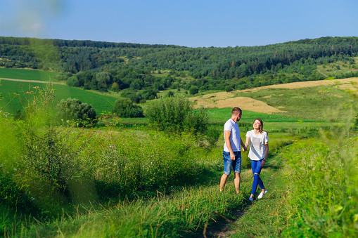 couple in love walking on a path in the middle of a field. meadow with green grass and forest. sunny day.