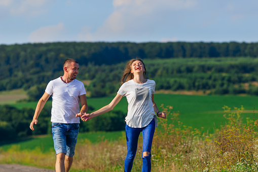 couple in casual clothes holding hands and running against forest and meadow background. walk.