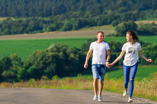 couple holding hands and running against the background of meadow and forest.