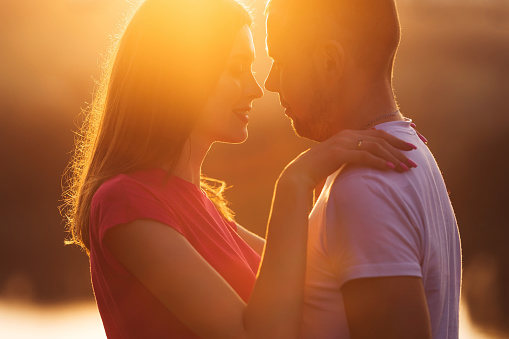 young, happy, loving couple, at sunset, standing in a green field, against the sky, in the arms, and looking at each other. close up.