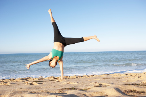 Young Woman In Fitness Clothing Turning Cartwheel Sandy On Beach