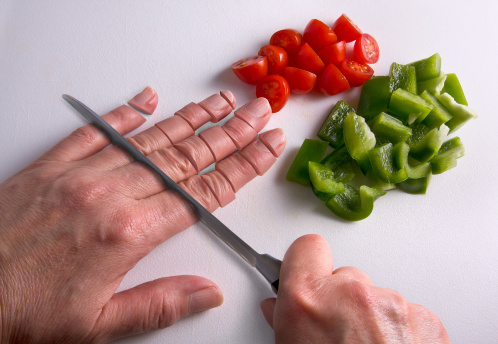 A human hand is being chopped with a knife on a cutting board.