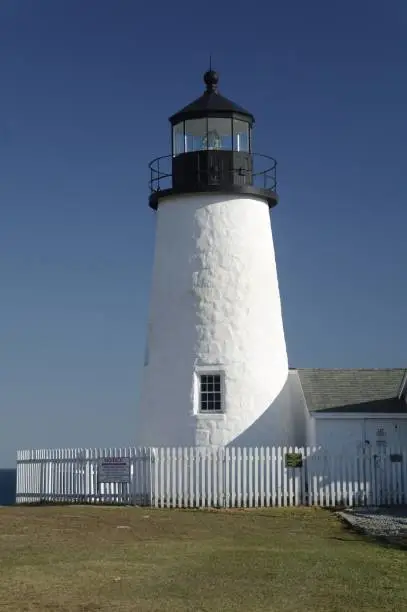 A white lighthouse, located at the end of a fenced-in coastal area